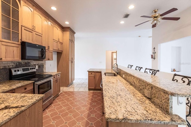 kitchen featuring sink, light stone counters, a kitchen breakfast bar, and stainless steel electric range