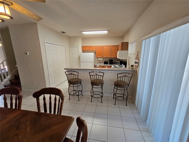 kitchen with light tile patterned flooring, white appliances, a breakfast bar, and kitchen peninsula