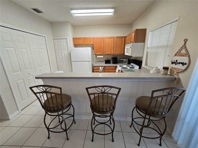 kitchen with a breakfast bar, a textured ceiling, light tile patterned floors, kitchen peninsula, and white appliances