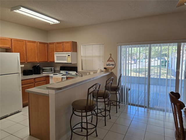 kitchen with light tile patterned flooring, a breakfast bar, a textured ceiling, kitchen peninsula, and white appliances