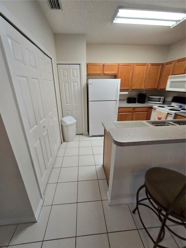 kitchen with light tile patterned floors, white appliances, a kitchen breakfast bar, and kitchen peninsula