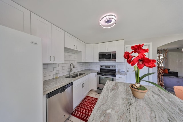 kitchen with appliances with stainless steel finishes, white cabinetry, sink, light tile patterned floors, and light stone counters