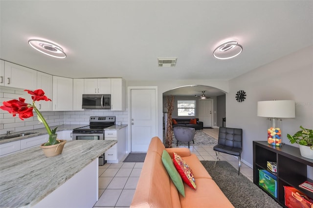 kitchen featuring stainless steel appliances, light tile patterned floors, decorative backsplash, and white cabinets