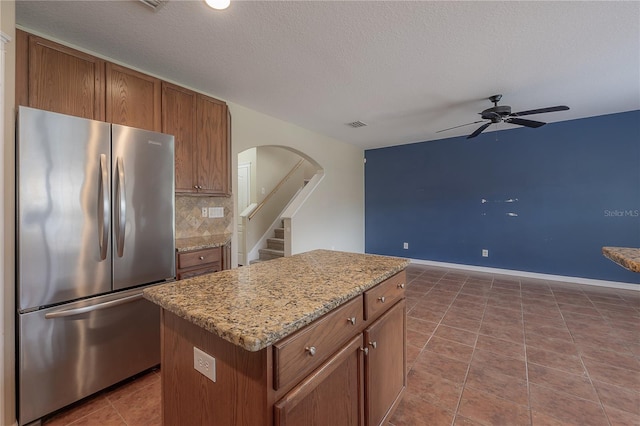 kitchen with backsplash, stainless steel fridge, a center island, ceiling fan, and a textured ceiling