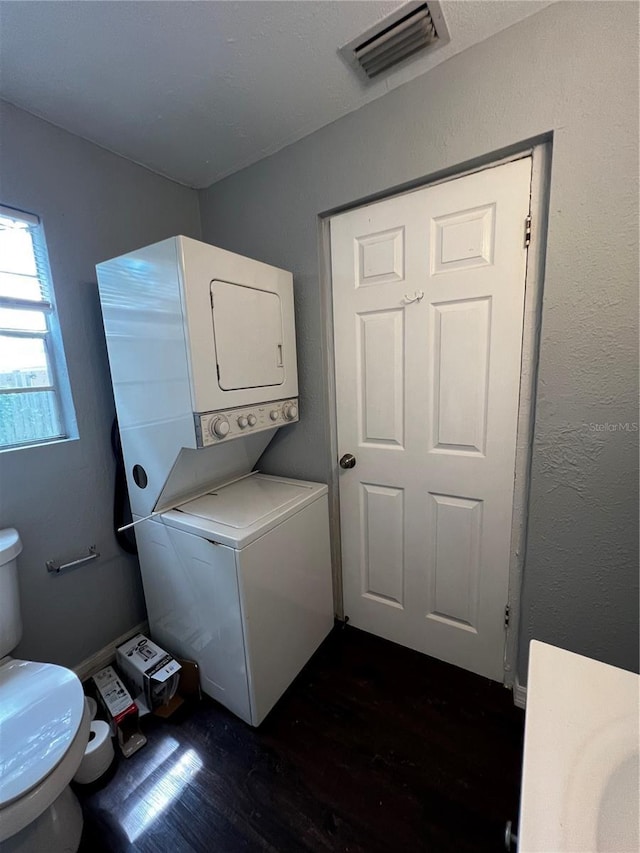 laundry room featuring stacked washing maching and dryer and dark hardwood / wood-style flooring