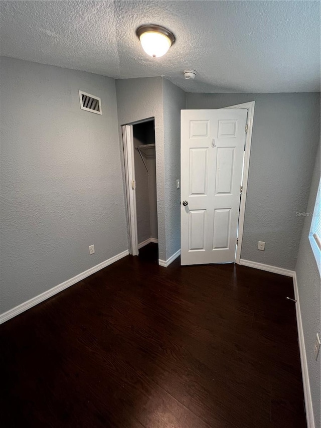 unfurnished bedroom with dark hardwood / wood-style flooring, lofted ceiling, a closet, and a textured ceiling