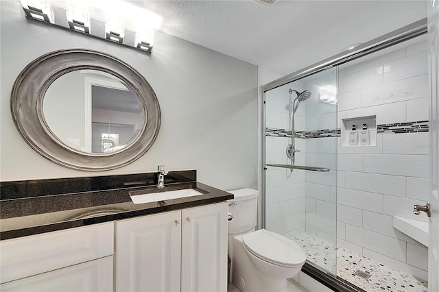 bathroom with vanity, toilet, a shower with door, and a textured ceiling