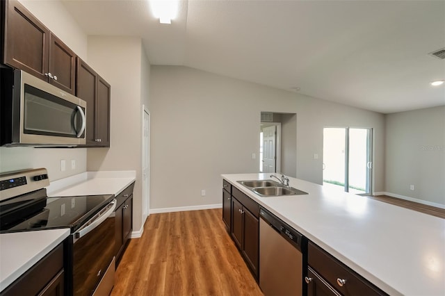 kitchen with sink, vaulted ceiling, dark brown cabinets, light wood-type flooring, and stainless steel appliances