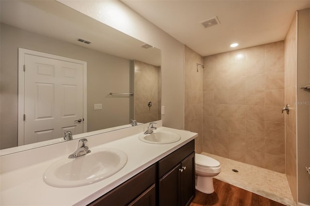 bathroom featuring hardwood / wood-style flooring, vanity, toilet, and a tile shower