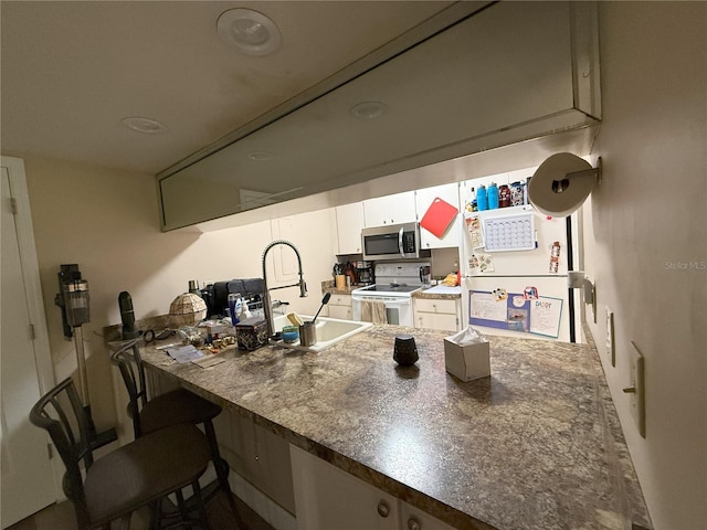 kitchen with a peninsula, a sink, white cabinetry, electric stove, and stainless steel microwave