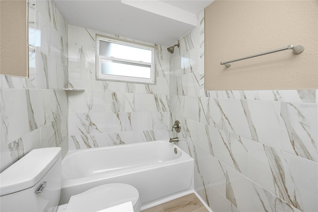 bathroom with tile walls, tiled shower / bath combo, and toilet