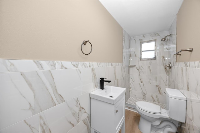 bathroom with hardwood / wood-style flooring, tile walls, tiled shower, vanity, and toilet