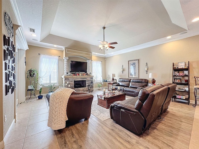 living room featuring a stone fireplace, light hardwood / wood-style floors, a raised ceiling, and a healthy amount of sunlight