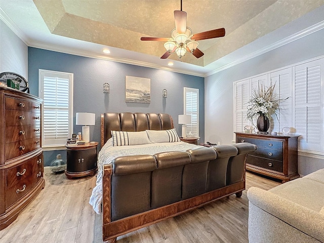 bedroom featuring ceiling fan, a tray ceiling, ornamental molding, a textured ceiling, and light wood-type flooring