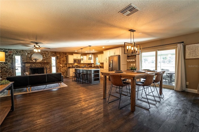 dining space with dark wood-style flooring, a fireplace, visible vents, a textured ceiling, and ceiling fan with notable chandelier