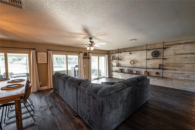 living room with a healthy amount of sunlight, wooden walls, visible vents, and dark wood finished floors