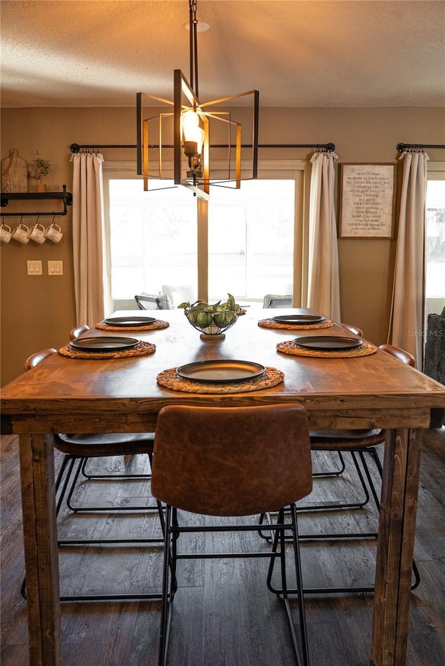 unfurnished dining area featuring a notable chandelier, a textured ceiling, dark wood finished floors, and a healthy amount of sunlight