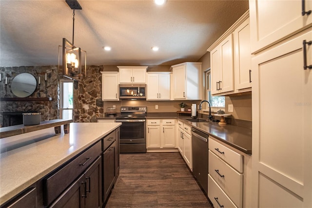 kitchen featuring stainless steel appliances, light countertops, hanging light fixtures, white cabinetry, and a sink