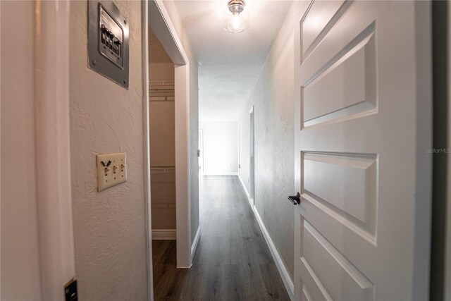 hall featuring dark wood-style floors, baseboards, and a textured wall