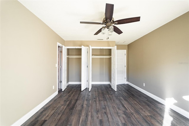 unfurnished bedroom with baseboards, dark wood-style flooring, and multiple closets