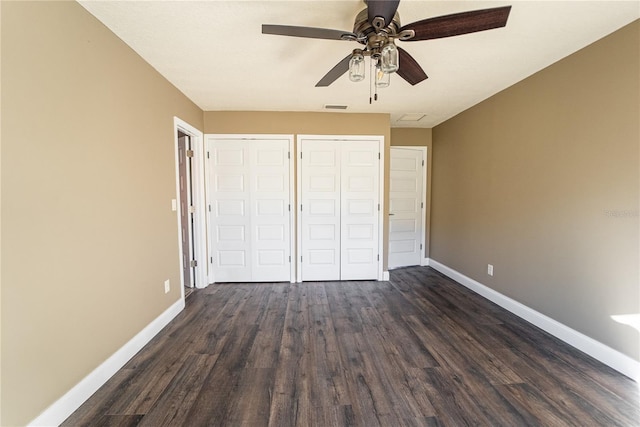 unfurnished bedroom with dark wood-type flooring, two closets, visible vents, and baseboards