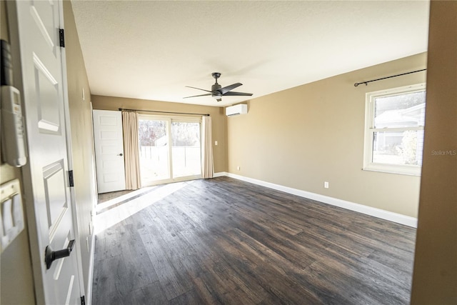 spare room featuring a wall unit AC, a ceiling fan, baseboards, and dark wood-style flooring