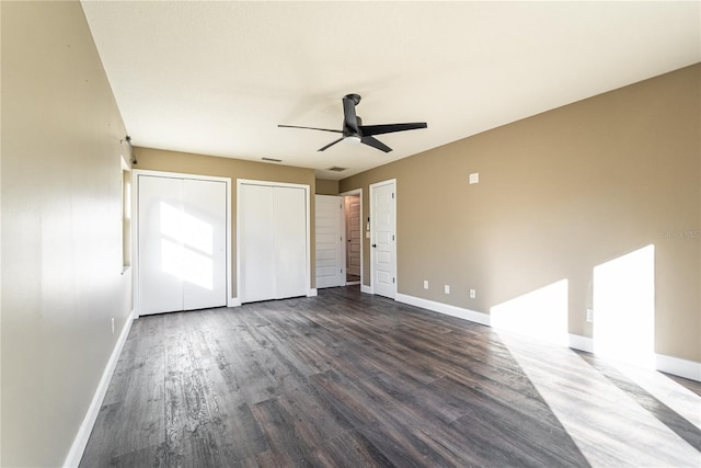 unfurnished bedroom featuring visible vents, baseboards, ceiling fan, wood finished floors, and two closets