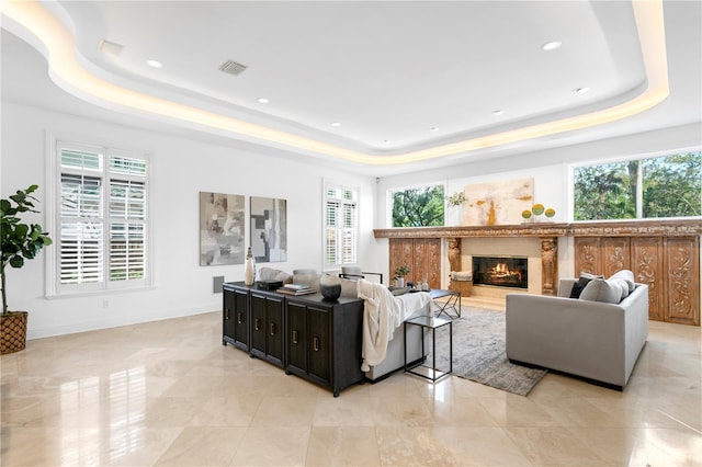 living room featuring a raised ceiling, a healthy amount of sunlight, and a fireplace