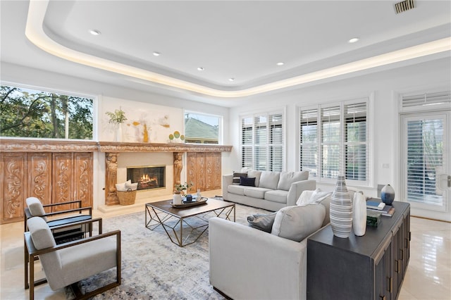 tiled living room featuring a fireplace, a healthy amount of sunlight, and a tray ceiling