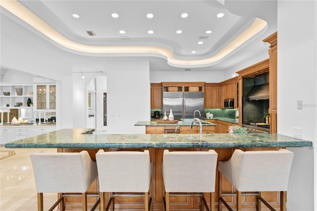 kitchen featuring stainless steel appliances, a kitchen breakfast bar, a raised ceiling, and kitchen peninsula