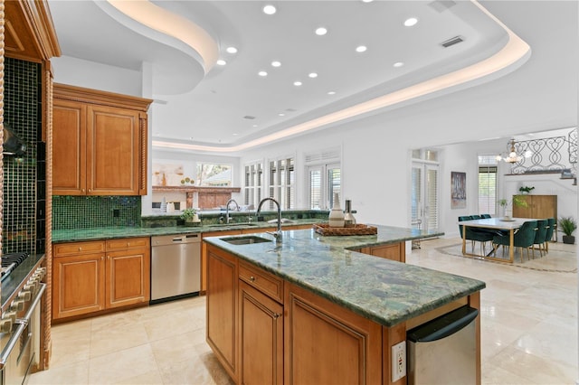 kitchen featuring stainless steel dishwasher, a raised ceiling, sink, and a center island with sink