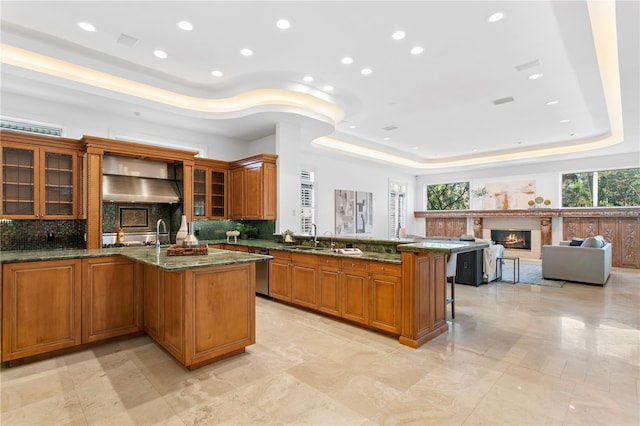 kitchen featuring a raised ceiling, a center island with sink, and dark stone countertops