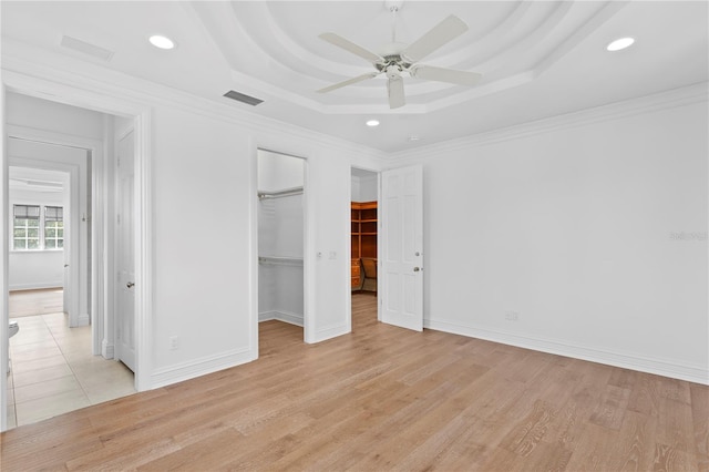 unfurnished bedroom featuring a spacious closet, light hardwood / wood-style flooring, ornamental molding, a raised ceiling, and ceiling fan