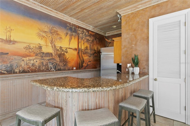 kitchen featuring stainless steel fridge, a kitchen bar, ornamental molding, light tile patterned floors, and kitchen peninsula