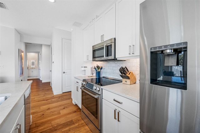 kitchen with light wood finished floors, visible vents, backsplash, appliances with stainless steel finishes, and white cabinets