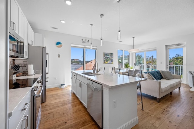 kitchen with a breakfast bar, a sink, light wood-style floors, appliances with stainless steel finishes, and an island with sink