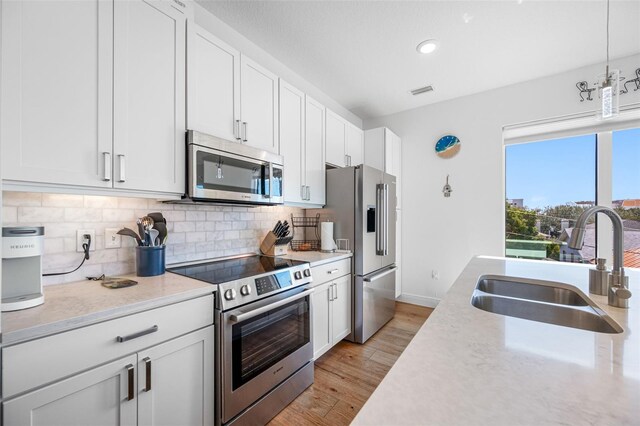 kitchen featuring light wood finished floors, backsplash, appliances with stainless steel finishes, white cabinets, and a sink