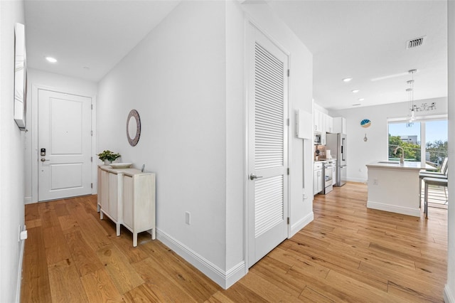 corridor with recessed lighting, a sink, visible vents, baseboards, and light wood-style floors