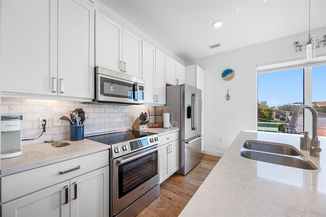 644 3rd Ave S Unit 305, Saint Petersburg, FL 33701 - kitchen featuring stainless steel appliances, decorative backsplash, white cabinets, light wood-style flooring, and pendant lighting