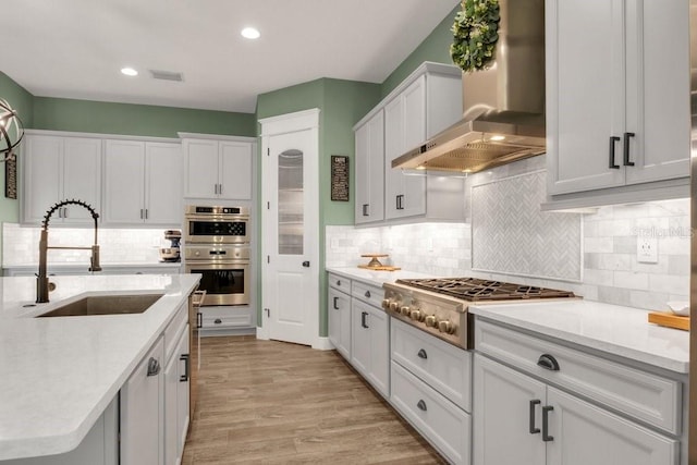 kitchen with wall chimney exhaust hood, stainless steel appliances, sink, and white cabinets