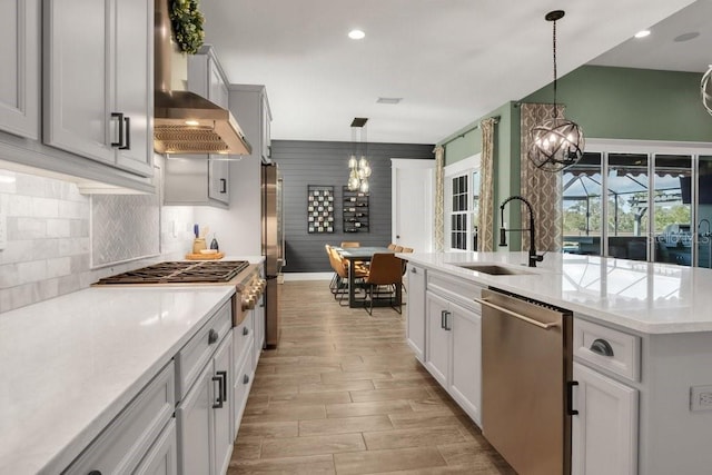 kitchen featuring sink, an inviting chandelier, decorative light fixtures, stainless steel appliances, and wall chimney range hood