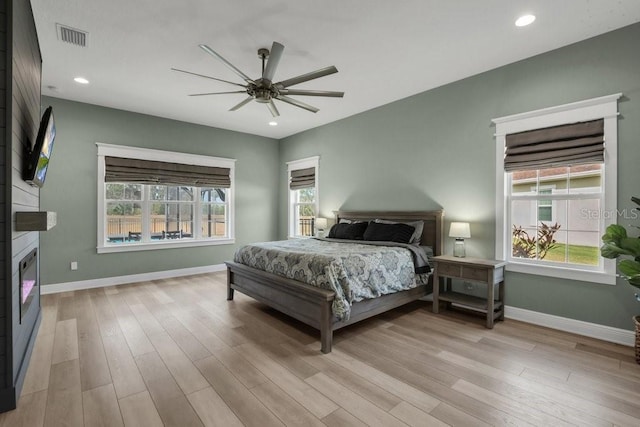 bedroom with multiple windows, ceiling fan, a fireplace, and light wood-type flooring