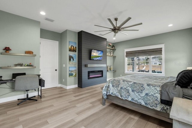 bedroom with light hardwood / wood-style flooring, a large fireplace, and ceiling fan