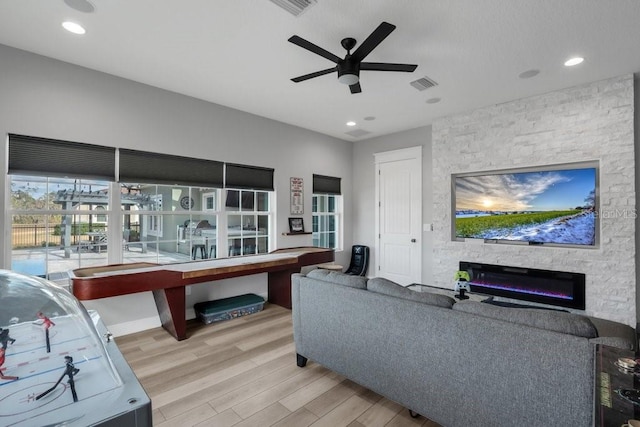 living room with ceiling fan, a stone fireplace, and light wood-type flooring