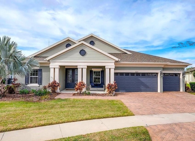 view of front of property featuring roof with shingles, stucco siding, decorative driveway, a front yard, and a garage