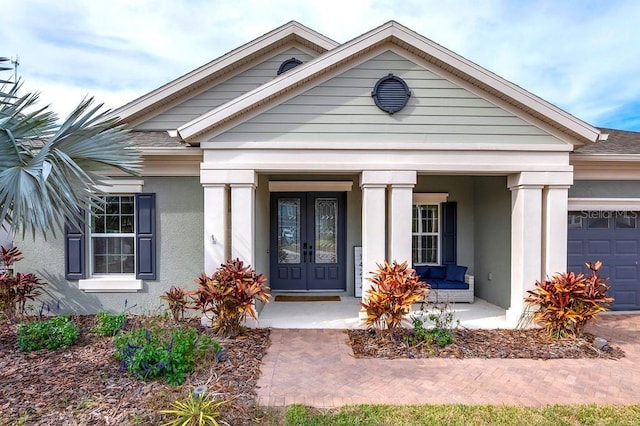 entrance to property featuring a garage, a porch, french doors, and stucco siding