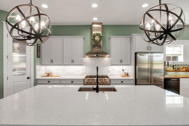 kitchen featuring an inviting chandelier, dishwasher, a sink, wall chimney range hood, and high end refrigerator