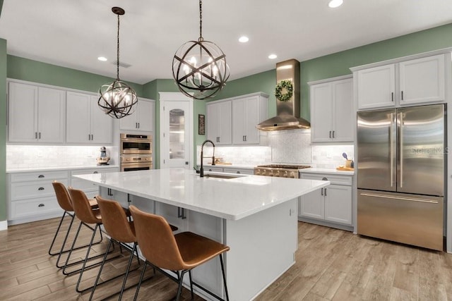 kitchen with wall chimney range hood, a chandelier, appliances with stainless steel finishes, a sink, and backsplash