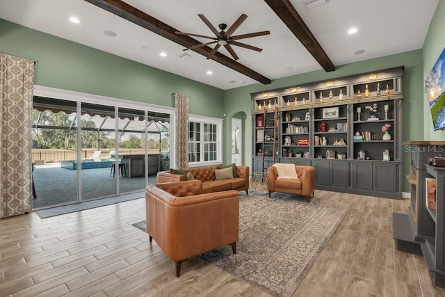 sitting room with beamed ceiling, ceiling fan, arched walkways, a high ceiling, and wood finished floors