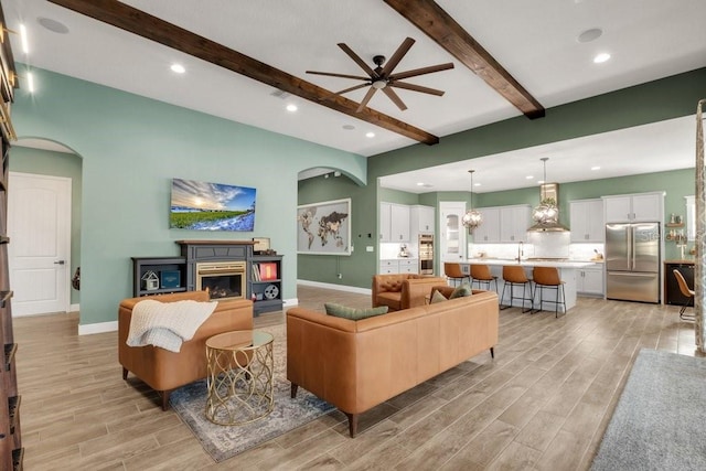 living area with light wood-type flooring, ceiling fan, beamed ceiling, and baseboards